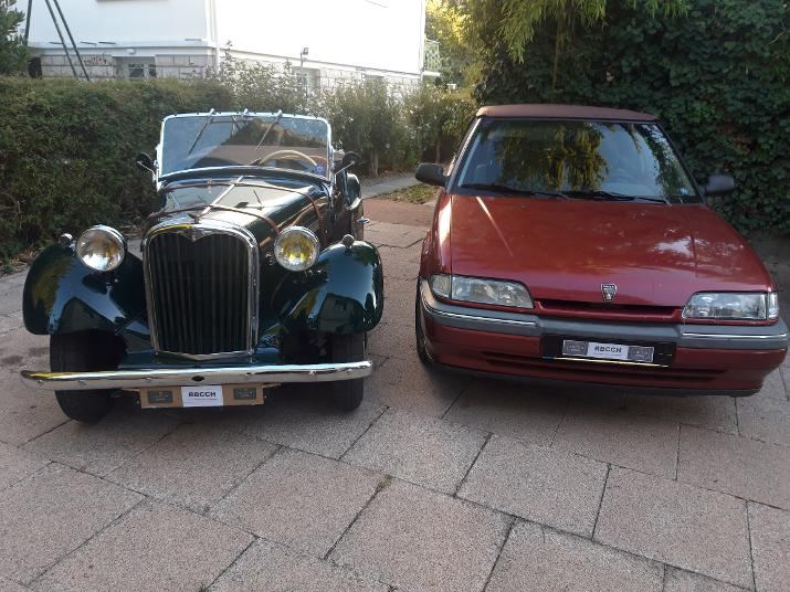 Un cabriolet anglais ancien vert et une Rover 214 rouge, côte à côte dans une allée, symbole du lien entre les anciennes et les Rover à moteur K